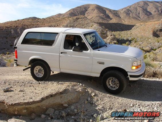 White 1996 Ford Bronco parked on a dirt road in a desert landscape