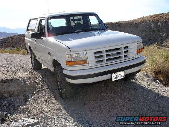White 1996 Ford Bronco parked on a dirt road with desert hills in background