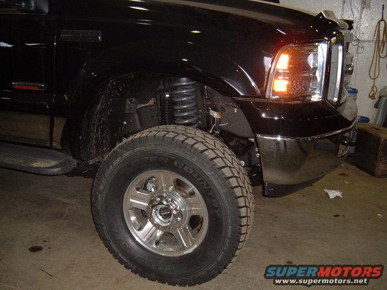 Front corner of black pickup truck, showing tire, suspension, and headlight