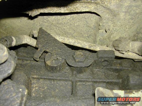 Underside view of greasy vehicle components with a rusty metal bracket and bolts