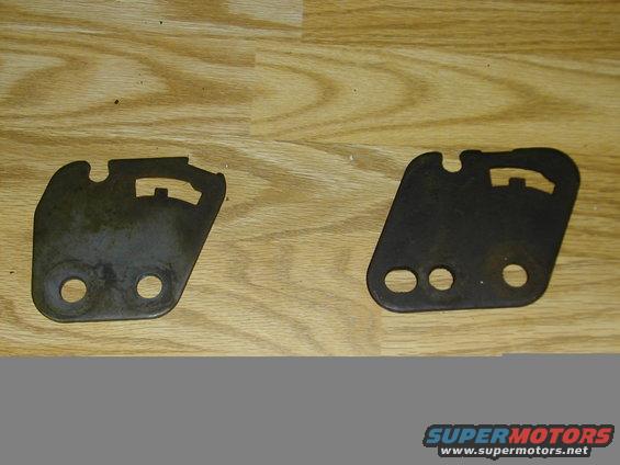 Two dark metal brackets with cutouts and holes on a wooden surface