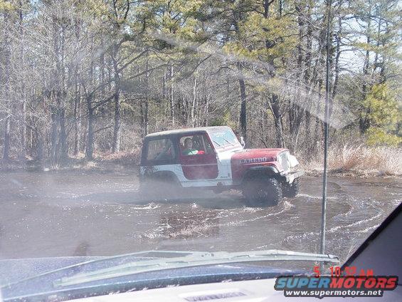 Red and white Jeep Wrangler Laredo driving through water