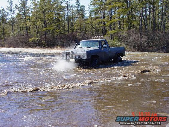 Pickup truck splashing through shallow water with snorkel and extra lights