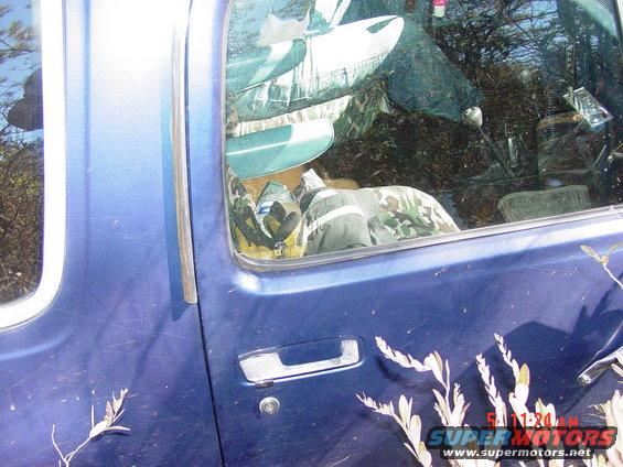 Interior of a blue pickup truck with camouflage gear and a stick shift visible