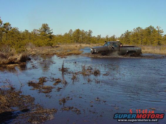 Dark-colored pickup truck driving through a muddy swamp, snorkel visible