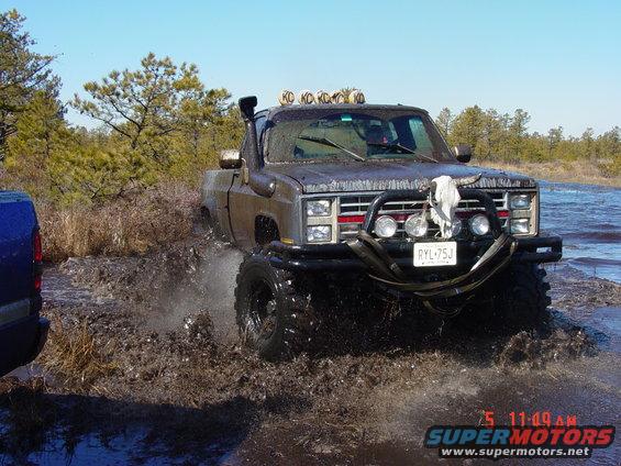Brown pickup truck with snorkel and bull bar driving through mud. License plate RYL-75J