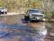 1995 Dodge 1500 - A dark blue Dodge Ram pickup truck navigates through a shallow water crossing, with another off-road vehicle visible in the background.