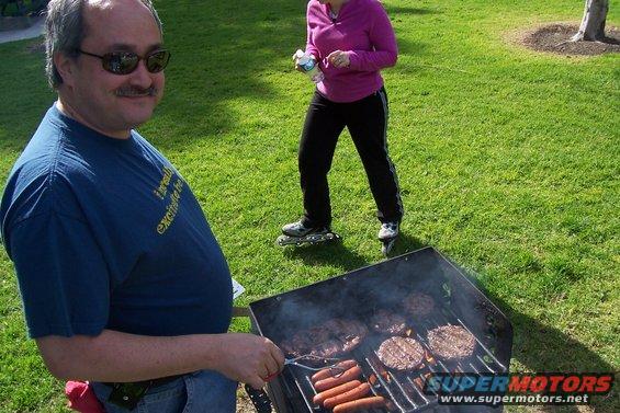 Man in blue t-shirt grilling hot dogs and hamburgers on a barbecue in a park
