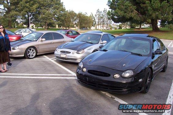 Black 1998 Mercury Sable in foreground, silver sedan with black hood behind it, tan sedan to the left