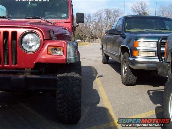 Front view of a red Jeep next to a dark green pickup truck. Text on the Jeep reads 'KCJeepClub.org'