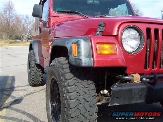 Red Jeep Wrangler front fender and tire, showing off-road tire and black rim