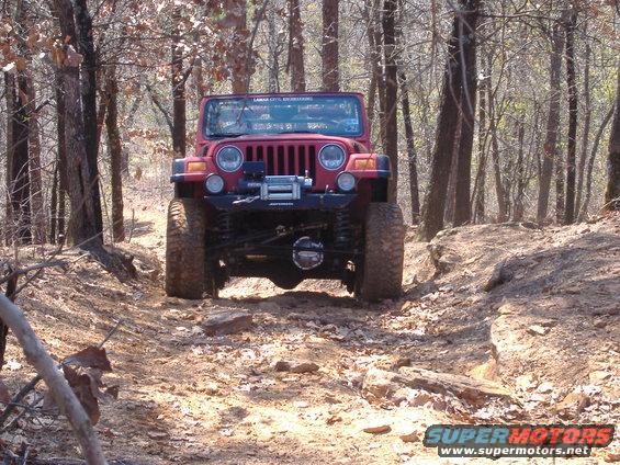 Red Jeep TJ on a rocky, wooded trail. It has a winch on the front bumper