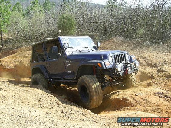 Blue Jeep Wrangler TJ model with lifted suspension and large tires navigating an off-road trail