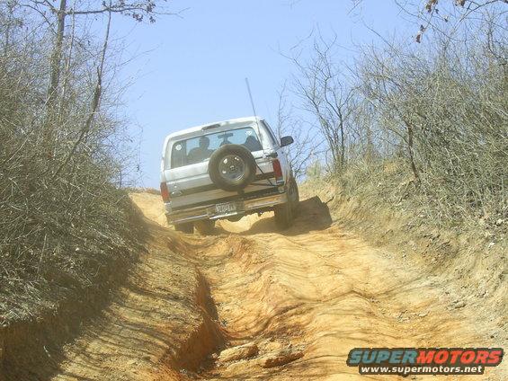 White SUV with spare tire on back driving up a dirt hill off-road