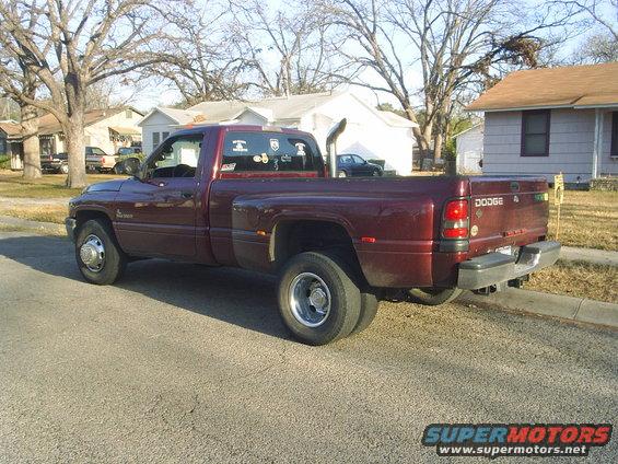 Maroon Dodge dually pickup truck with dual rear wheels, large exhaust stack, and aftermarket stickers on the rear window