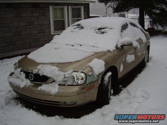 Gold sedan covered in snow, front 3/4 view. Appears to be a Mercury Sable