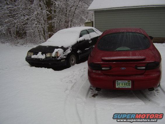 red Ford Taurus rear end, black sedan covered in snow next to it
