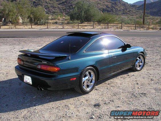 Teal 1993 Mazda MX-6 coupe with a rear spoiler and sunroof, parked on a gravel lot