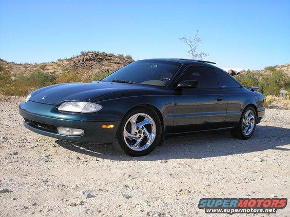 Dark green 1993 Mazda MX-6 coupe with chrome wheels parked on a dirt road
