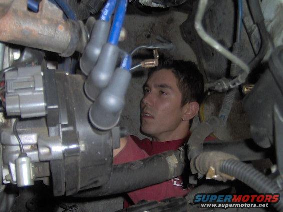 Man in red shirt working on engine components, including spark plug wires and distributor
