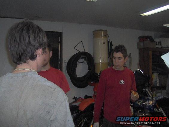 Three guys in a garage, one eating pizza