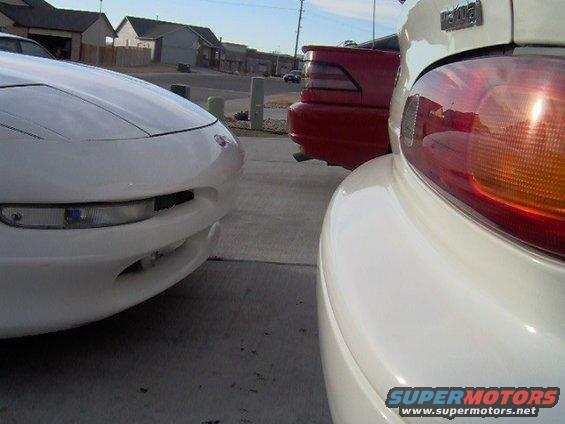 White car front end with pop-up headlight housing, red car rear end with spoiler, and white car tail light visible
