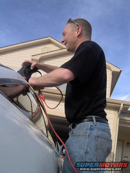 Man plugging charger into side of car. House and garage in background