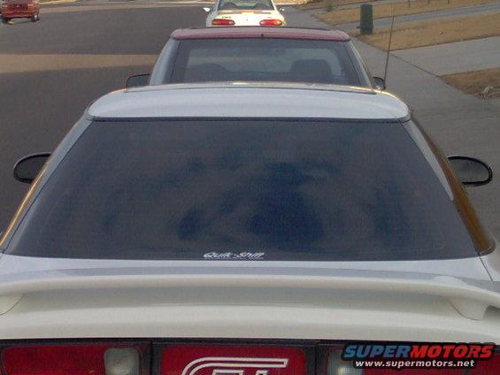 White coupe with a rear spoiler and tinted windows, seen from behind