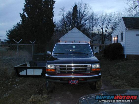 Black Ford F-Series truck with a red stripe on the grille, facing forward. A trailer is to its left