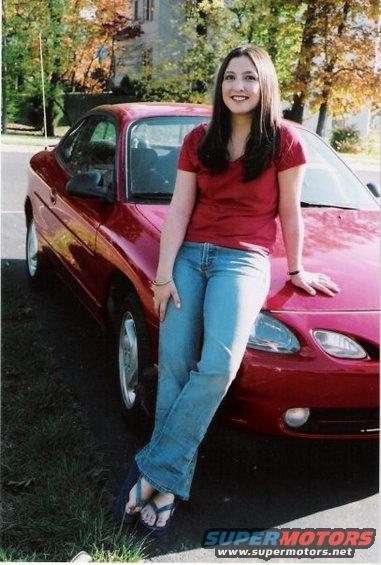 Red 1995 Ford Probe coupe, 3/4 front view, with a woman leaning on the hood