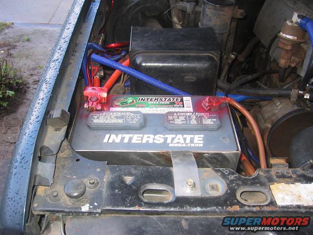 Vehicle battery with red and blue cables in engine bay. Interstate Mega-Tron battery