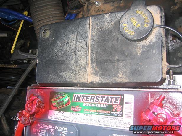 Vehicle engine bay showing an Interstate Mega-Tron 75 battery and a black cover with a yellow washer fluid cap