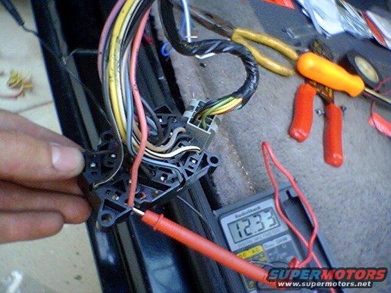 Close-up of a vehicle wiring harness with a multimeter reading 12.33V