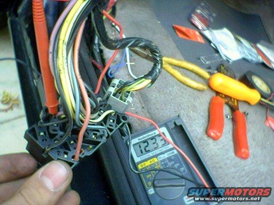 Close-up of vehicle wiring harness with multimeter reading 12.33V