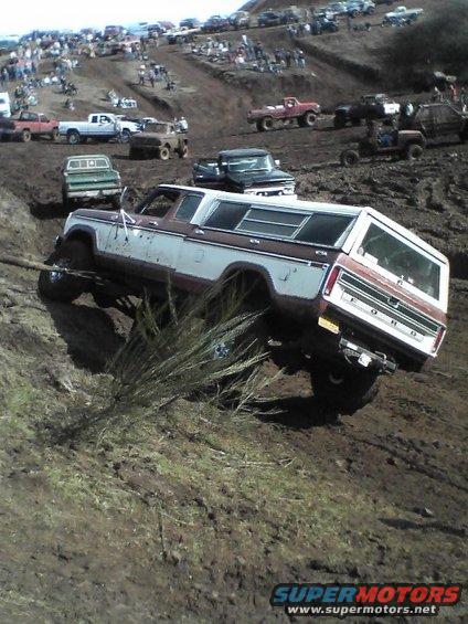 Ford Bronco with camper shell climbing a muddy hill, crowd watching