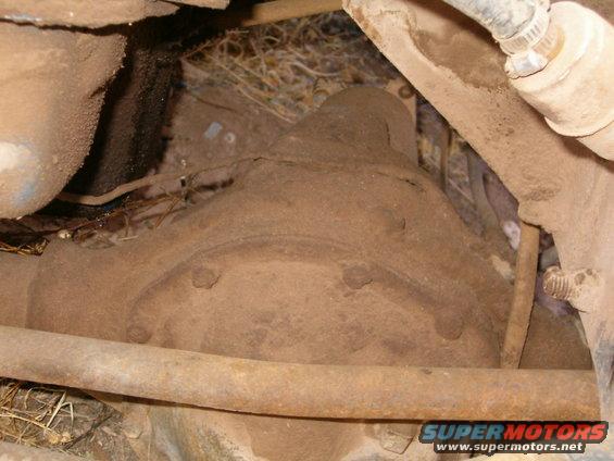 Rear axle housing covered in dirt and rust, with surrounding suspension components