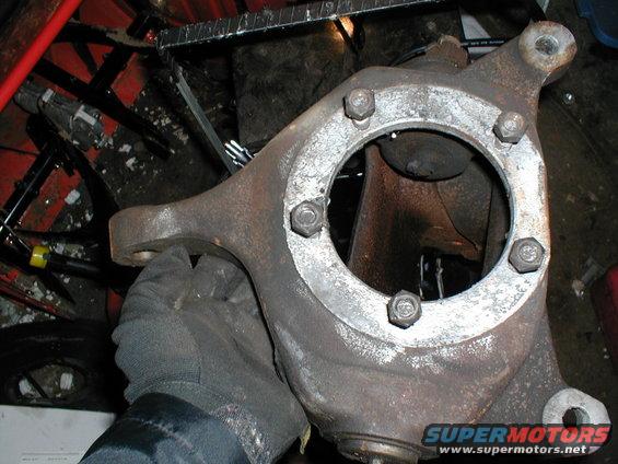 Rusty metal suspension part held by a gloved hand, Supermotors.net logo visible
