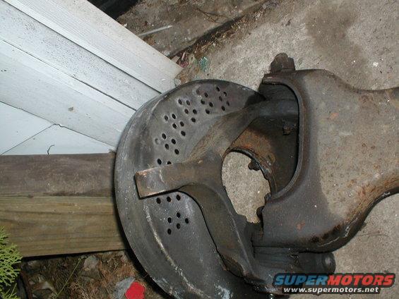 Close-up of a vehicle's brake rotor with drilled holes and a rusty suspension part