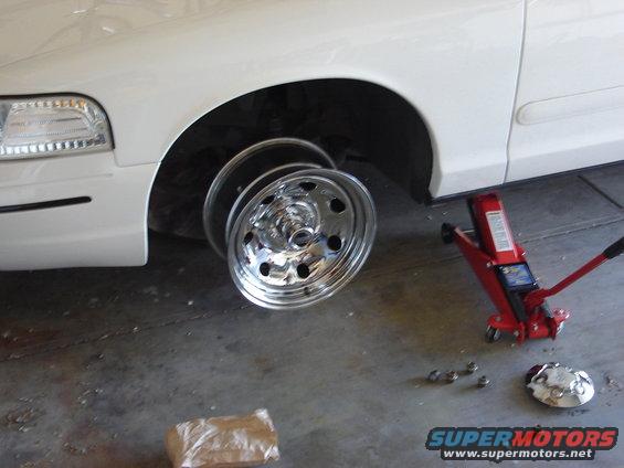 White 2000 Ford Crown Victoria side view, front wheel removed, on a red hydraulic jack