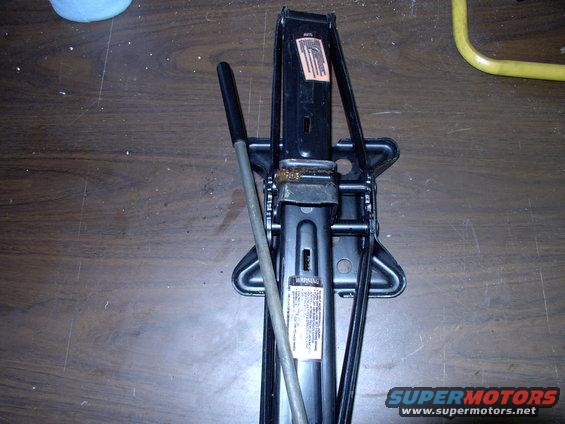 Black scissor jack with a metal handle on a wooden surface