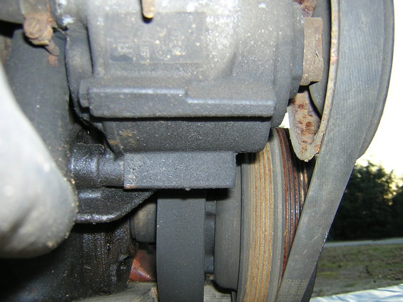 Engine part with greasy black casing, multiple pulleys, and a V-belt. Some rust is visible on a pulley edge