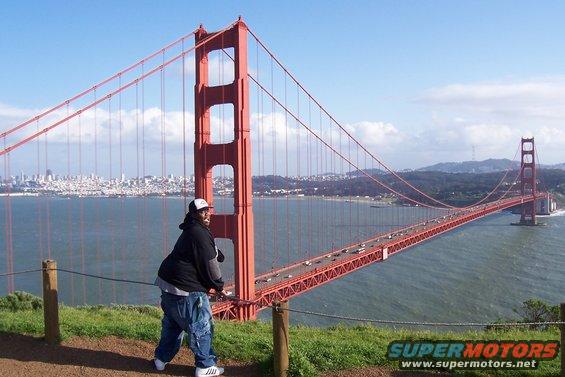 Man in baggy jeans and hoodie stands on a hill overlooking the Golden Gate Bridge with San Francisco skyline in the background
