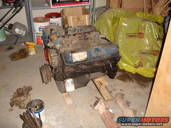 V8 engine on wooden blocks, with exhaust manifolds and other parts nearby