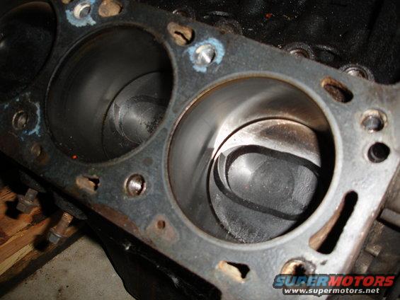 Engine block with two cylinders visible, showing pistons inside. Some rust and wear are present