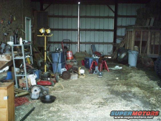 Barn interior with tools, lawnmower, and hay on the floor. Metal shelving unit on the left