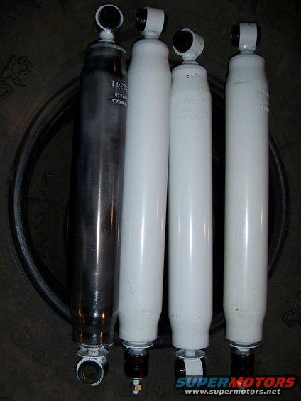 Four shock absorbers, one dark metal and three white, laid on a tire