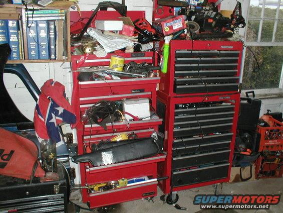 red tool chests overflowing with car parts and tools, a confederate flag hangs on the side of a car door