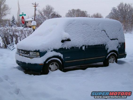 Teal van covered in snow, parked on a street with a stop sign