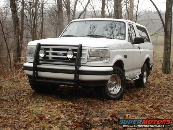 White Ford Bronco with bull bar and auxiliary lights parked on a wooded hill