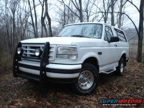 White 1995 Ford Bronco with bull bar parked in woods